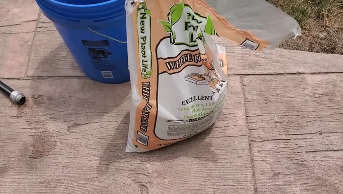 Pour half a bag of sand into the 5-gallon bucket.